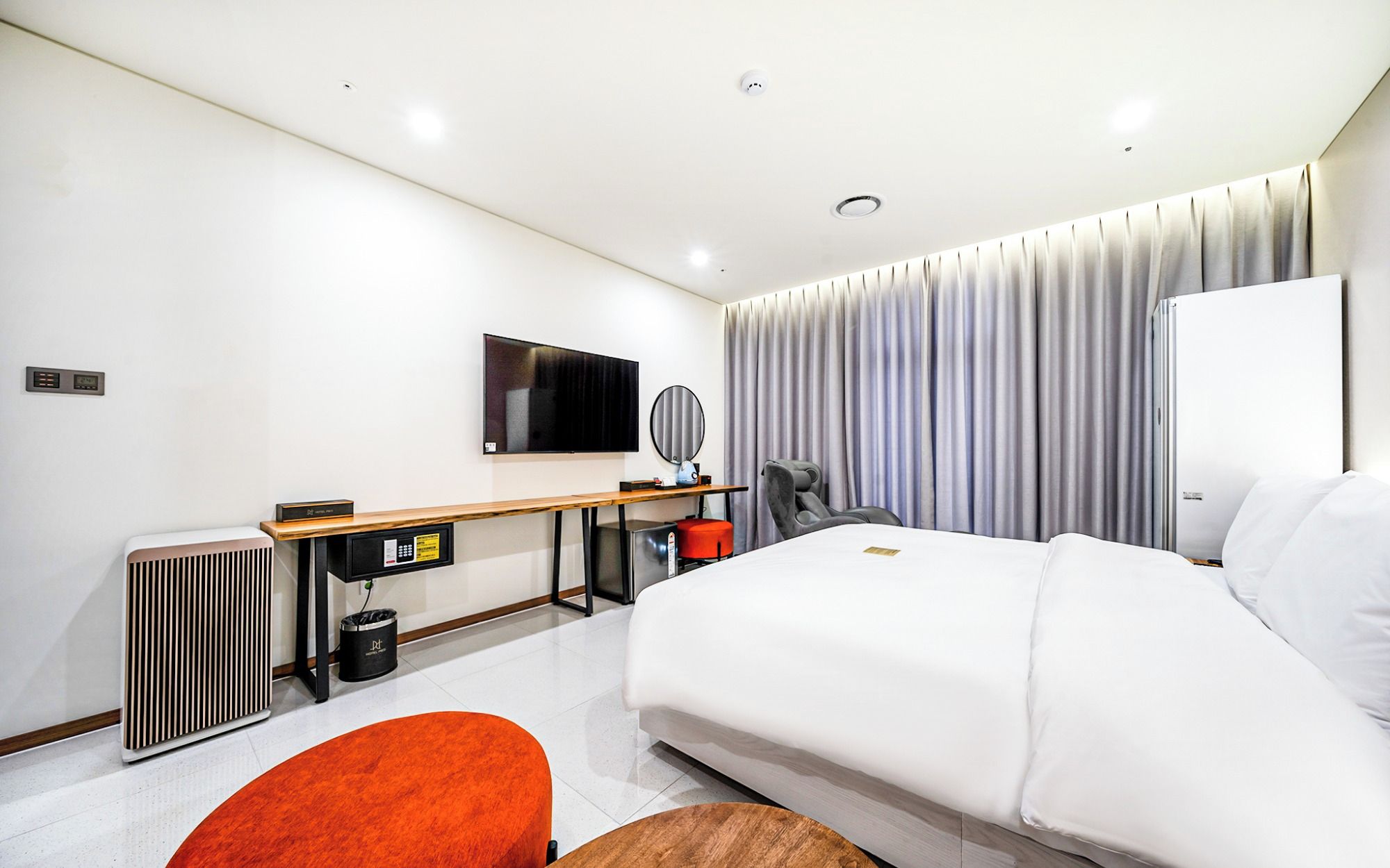 A modern hotel room with a bed, a desk, a television, and a large window with curtains.