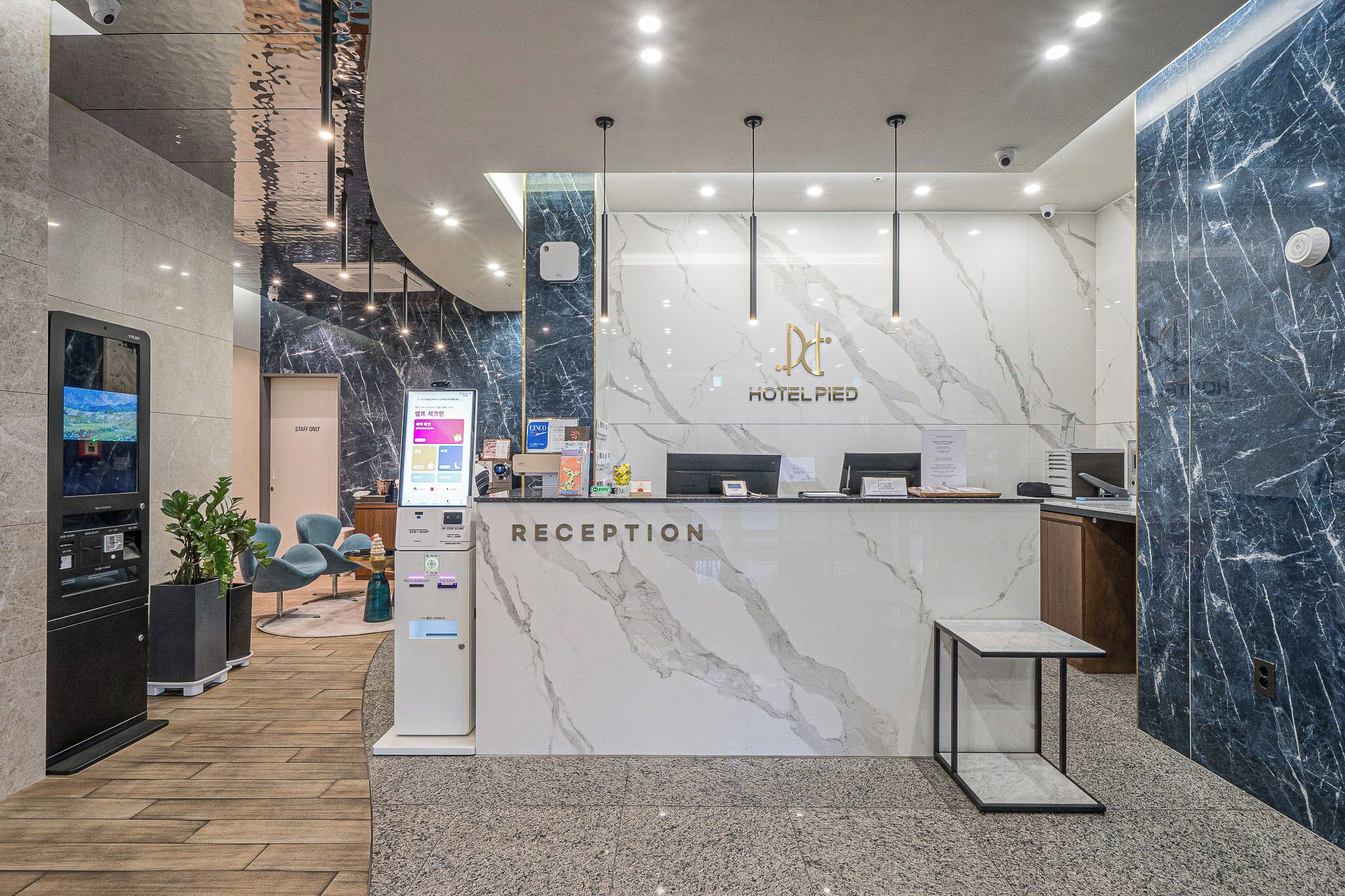 Zona de recepción de un hotel con mostrador de mármol, pantalla digital y escritorio para recepción.