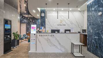 Zona de recepción de un hotel con mostrador de mármol, pantalla digital y escritorio para recepción.