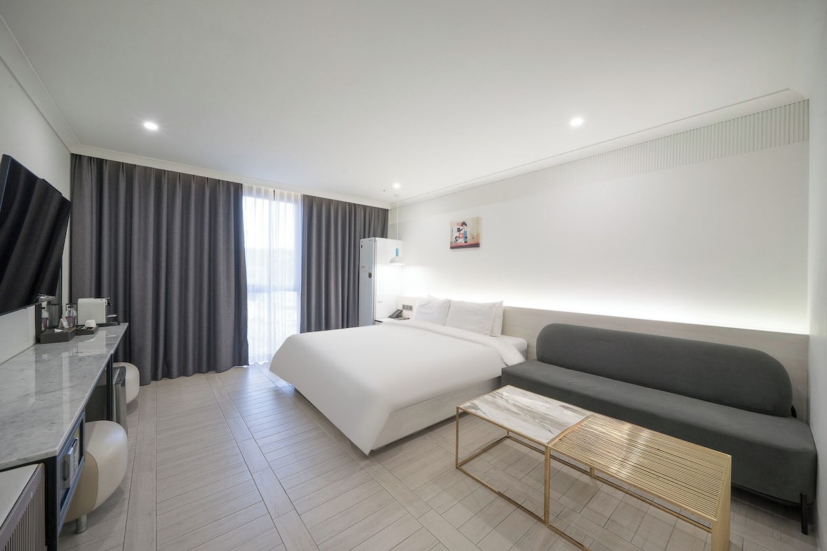 Una habitación de hotel moderna con cama, sofá, escritorio y una pequeña mesa.