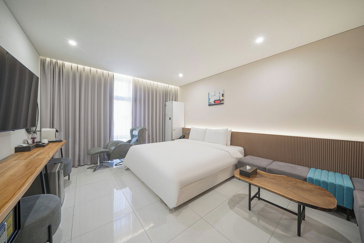 Una habitación de hotel moderna con una cama grande, un escritorio con silla, un sofá y una mesita.