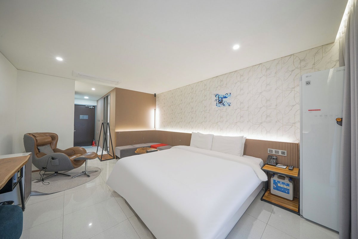 Una habitación de hotel moderna con una cama grande, un escritorio, una silla, un armario y una pequeña mesa con un teléfono y un control remoto.
