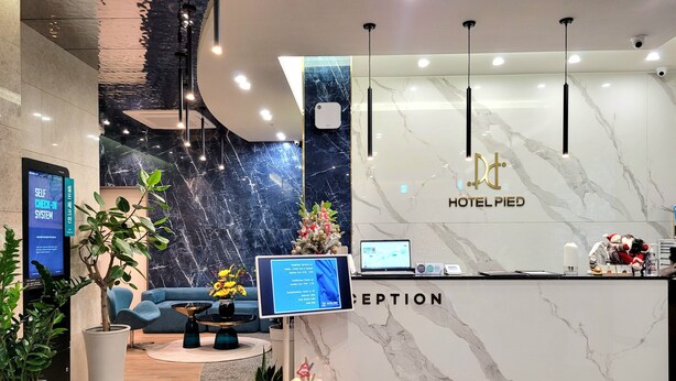 A hotel reception area with a marble wall, reception desk, computer monitors, and potted plants. - Hotel PIED Suseong (Daegu)