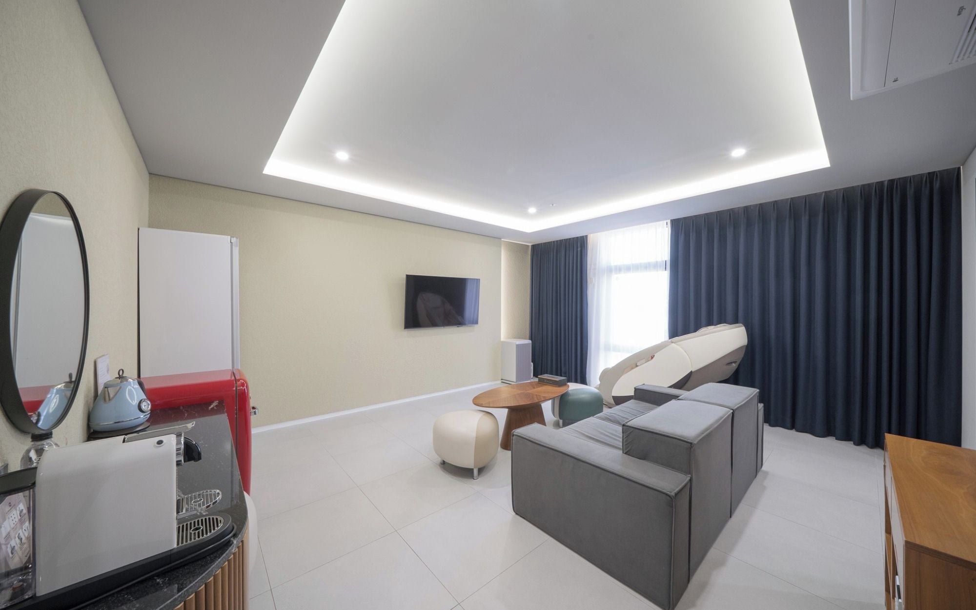 Ett modernt hotellrum med en platt-TV, en soffa, ett litet runt bord och en taklampa.