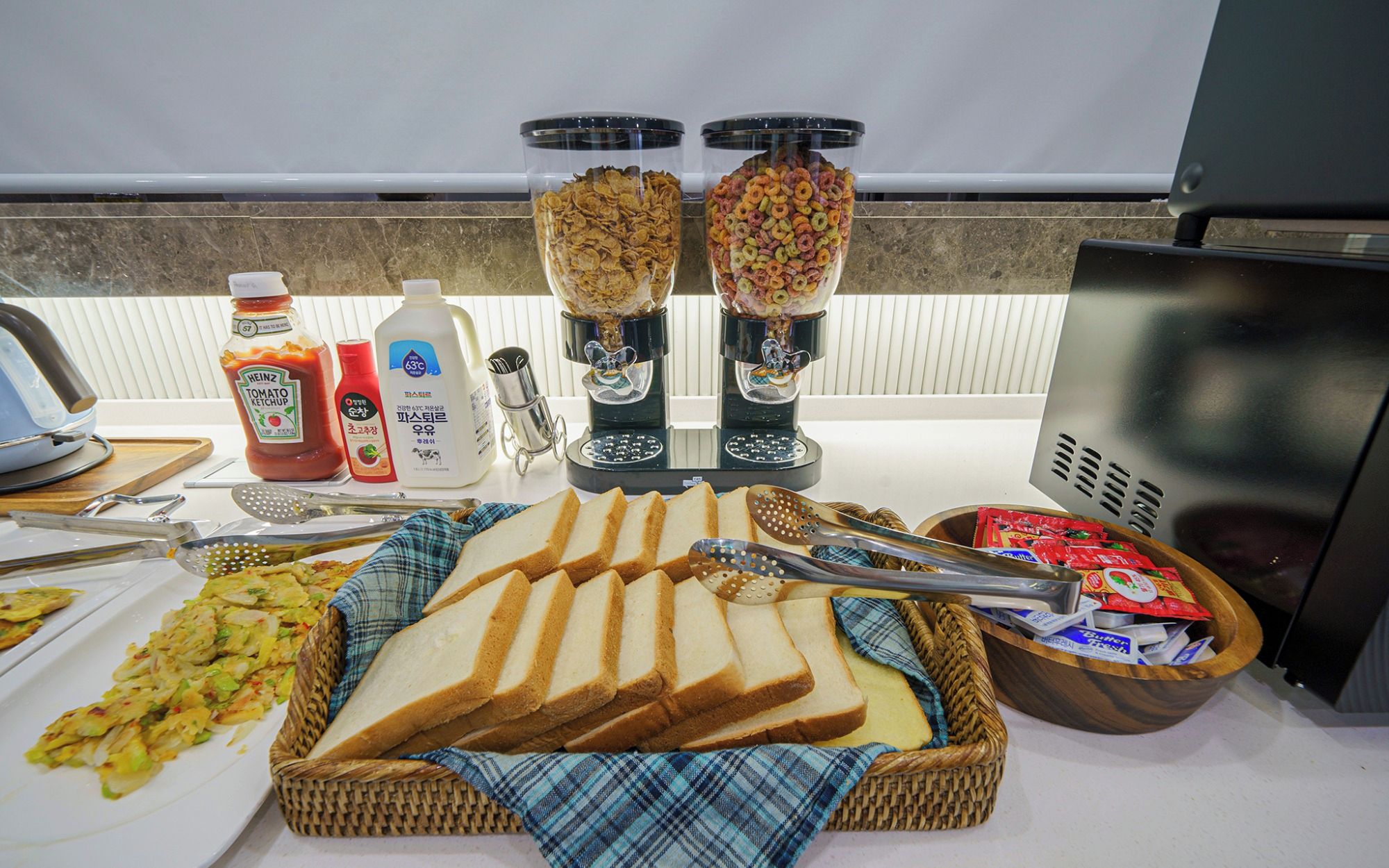 Un bufé de desayuno con pan, cereales, salsas y una máquina de café.