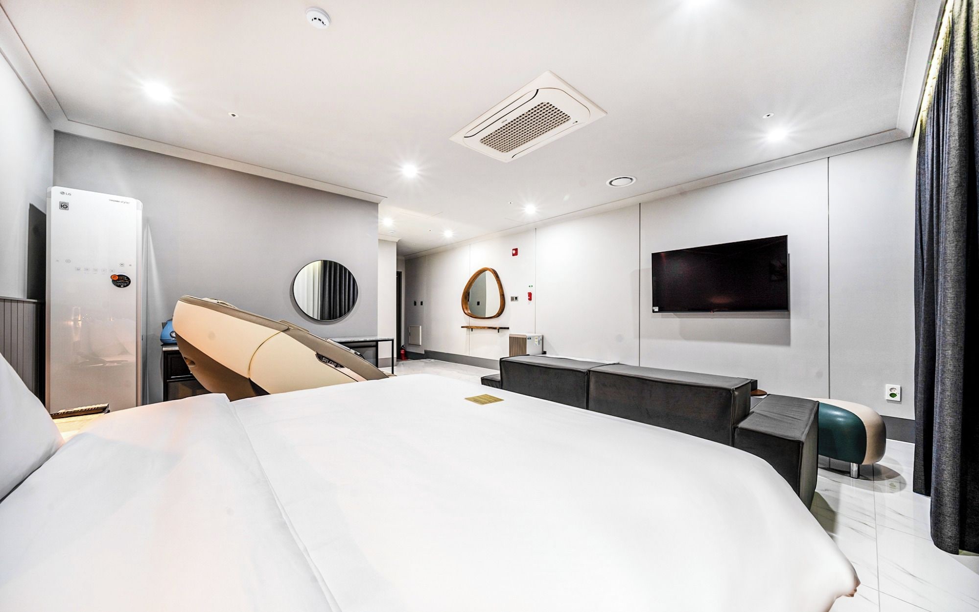 A modern hotel room with a large bed, a flat-screen TV mounted on the wall, a built-in heater, and a mirror.