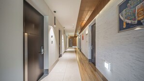 A modern hotel corridor with a wooden ceiling, light-colored walls, and a tiled floor. - Hotel PIED Suseong (Daegu)