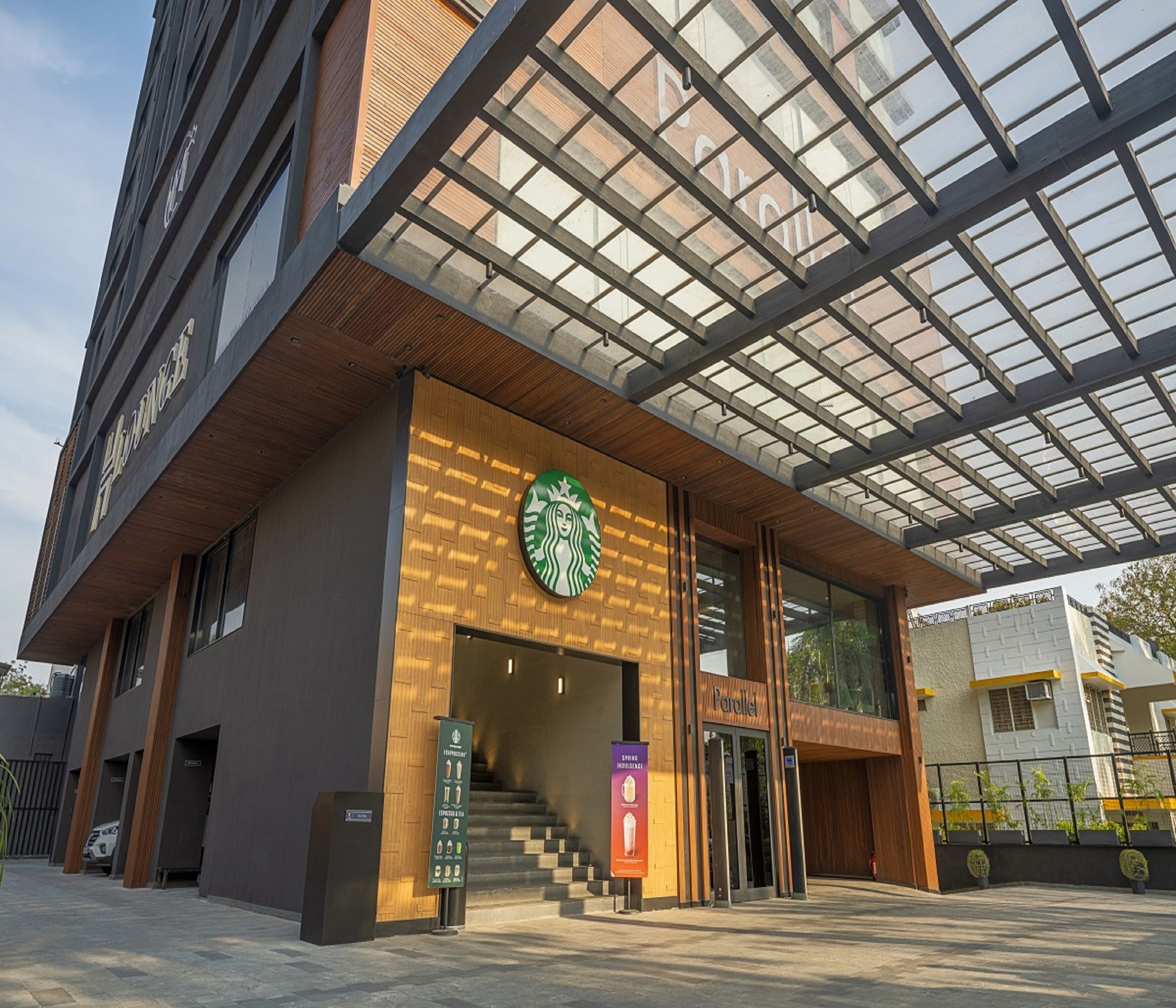 Ein modernes Gebäude mit Starbucks-Logo, einer Treppe, die zu einem Eingang führt, und einer Glasdachkonstruktion.