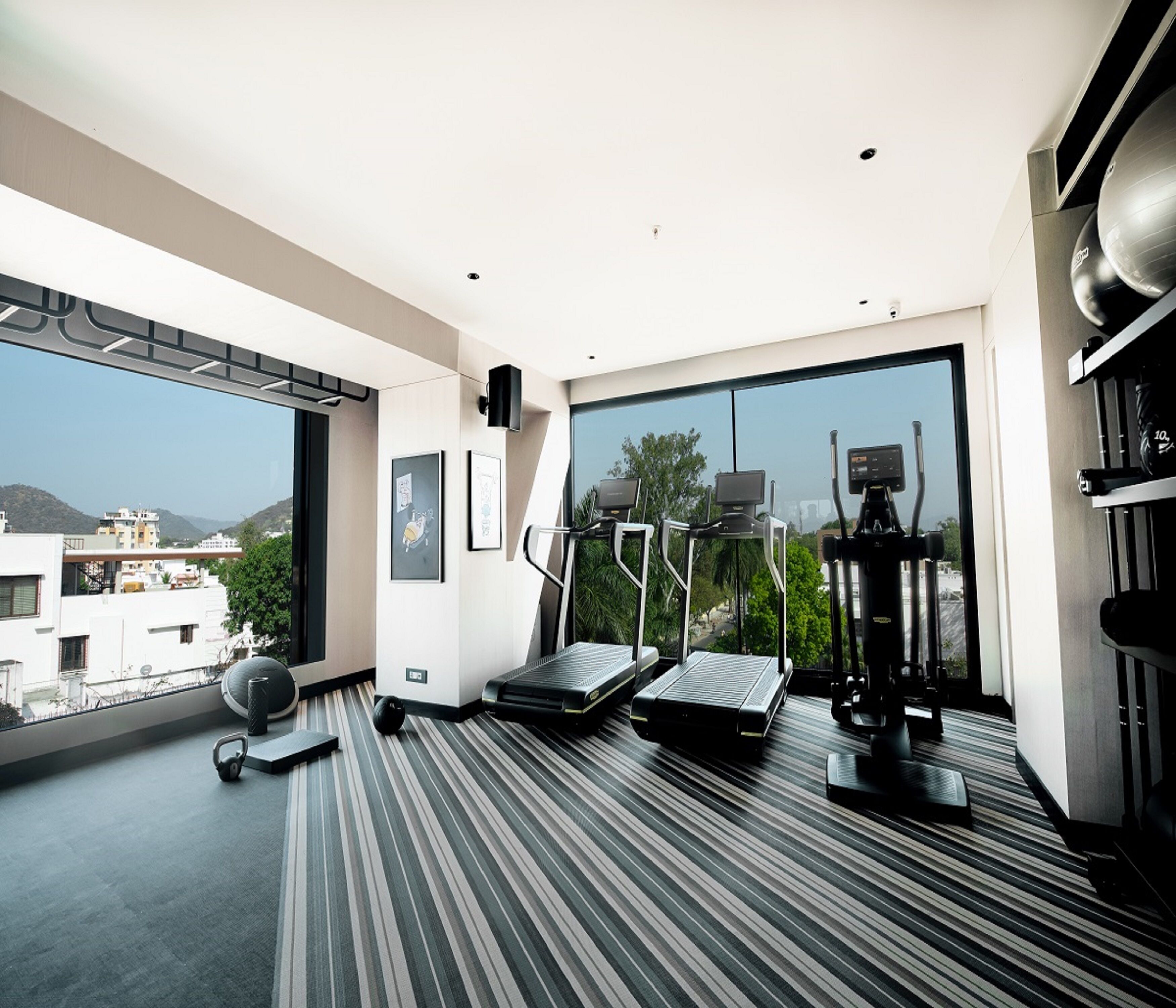 A modern hotel room with a large window, a treadmill, an elliptical machine, and a yoga mat.