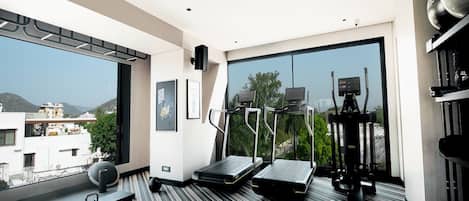 A modern hotel room with a large window, a treadmill, an elliptical machine, and a yoga mat.