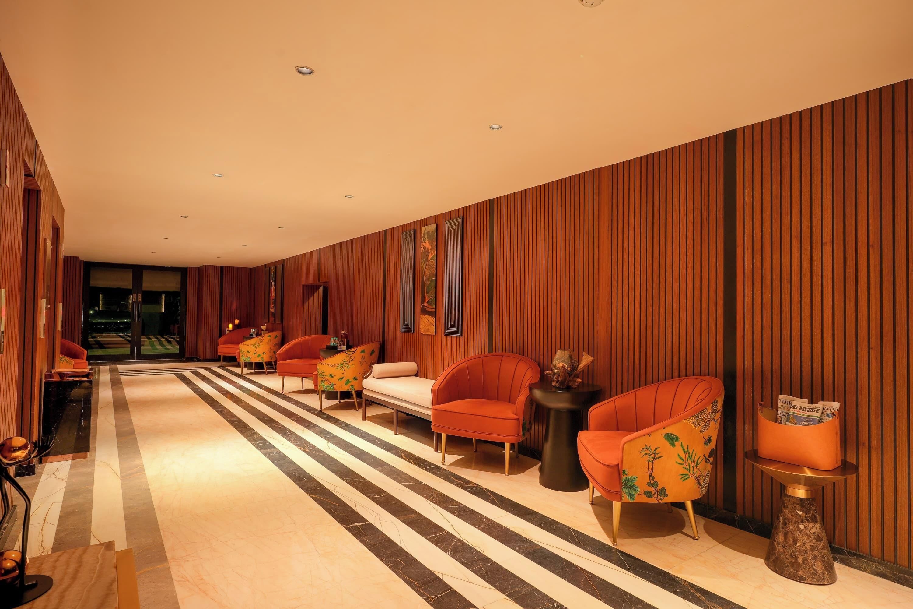 Um lobby moderno com piso listrado, painéis de madeira e poltronas laranja.