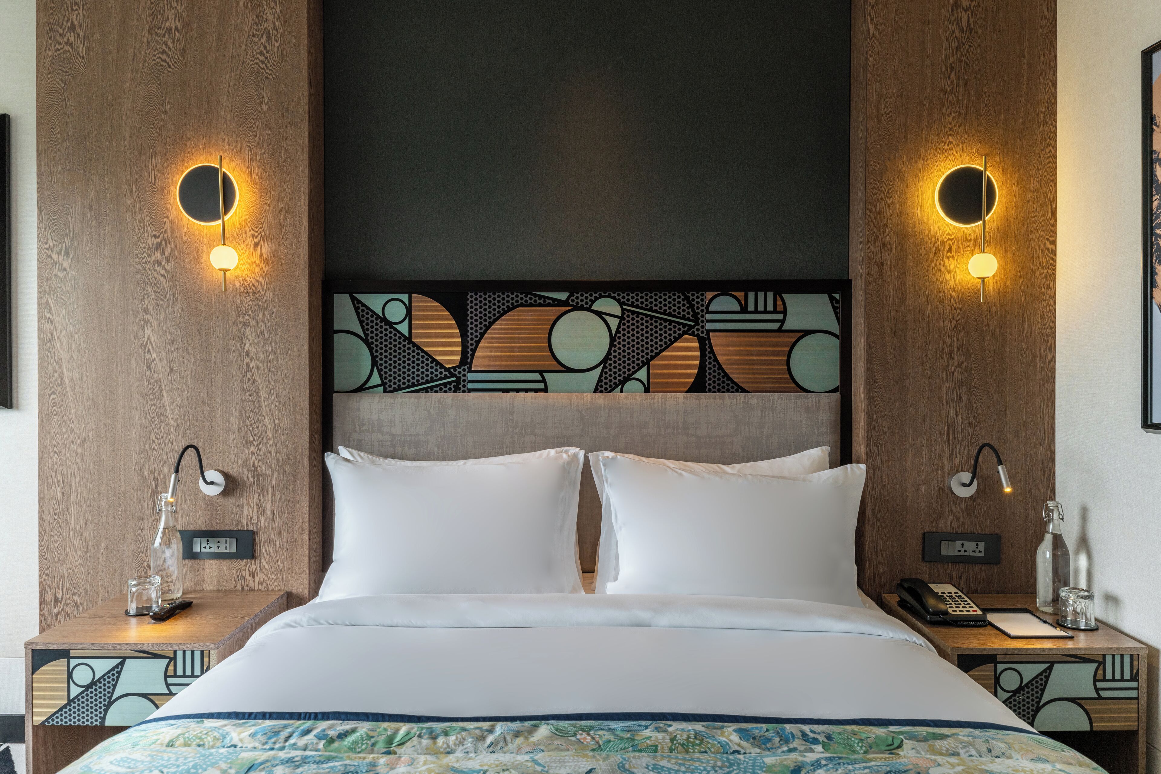 Una habitación de hotel moderna con una cama grande, dos mesitas de noche e iluminación en la pared.