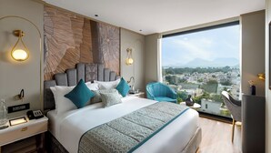 A modern hotel room with a large bed, a desk, and a view of a cityscape.