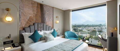 A modern hotel room with a large bed, a desk, and a view of a cityscape.