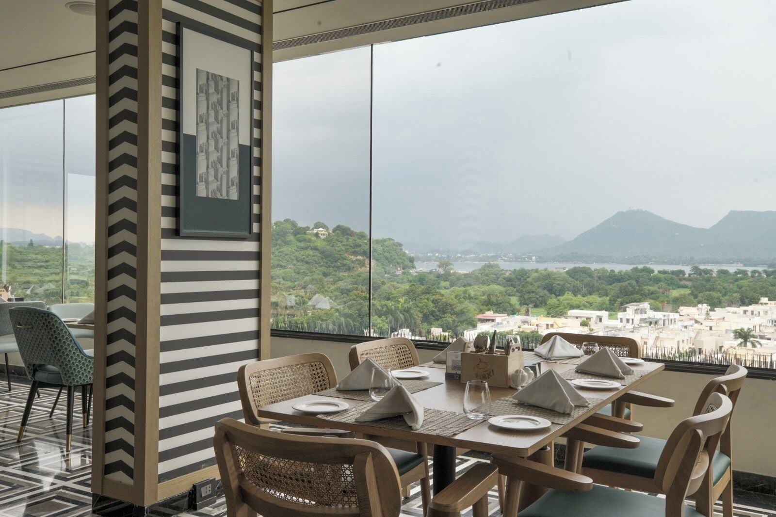 A dining area with a table set for four, large windows offering a view of a cityscape and mountains.