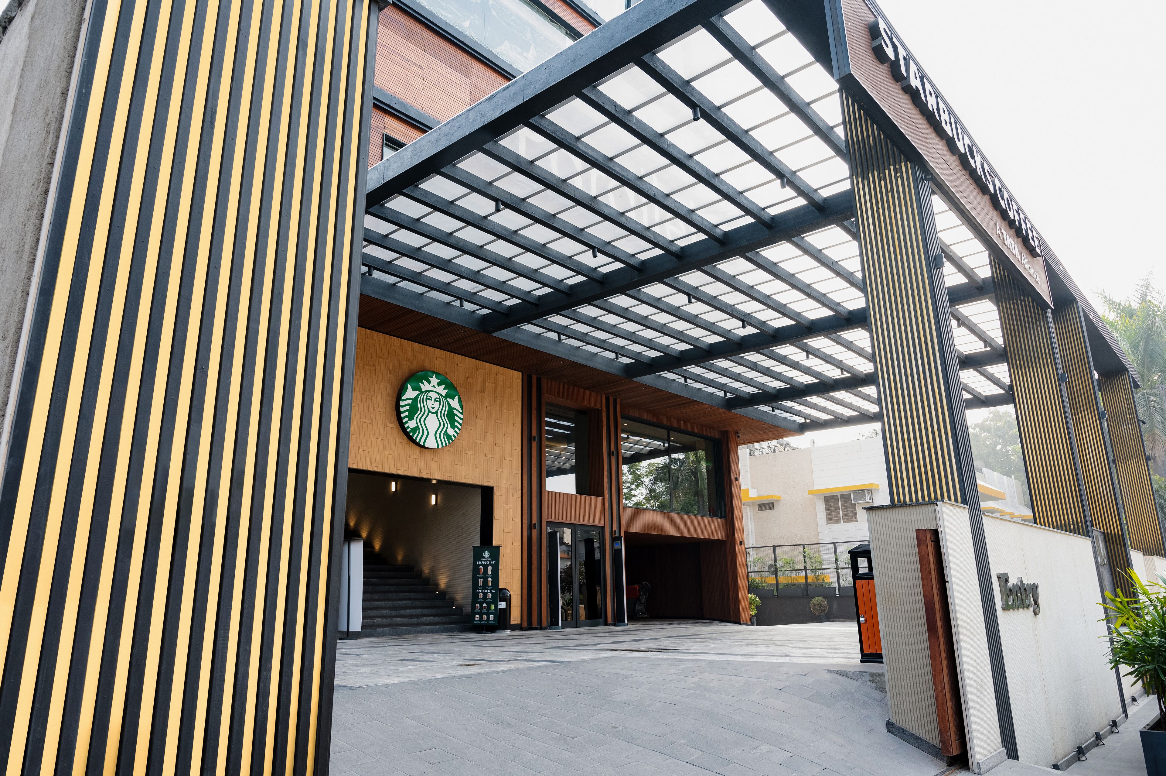 A modern Starbucks entrance with a wooden facade, glass doors, and a covered walkway.
