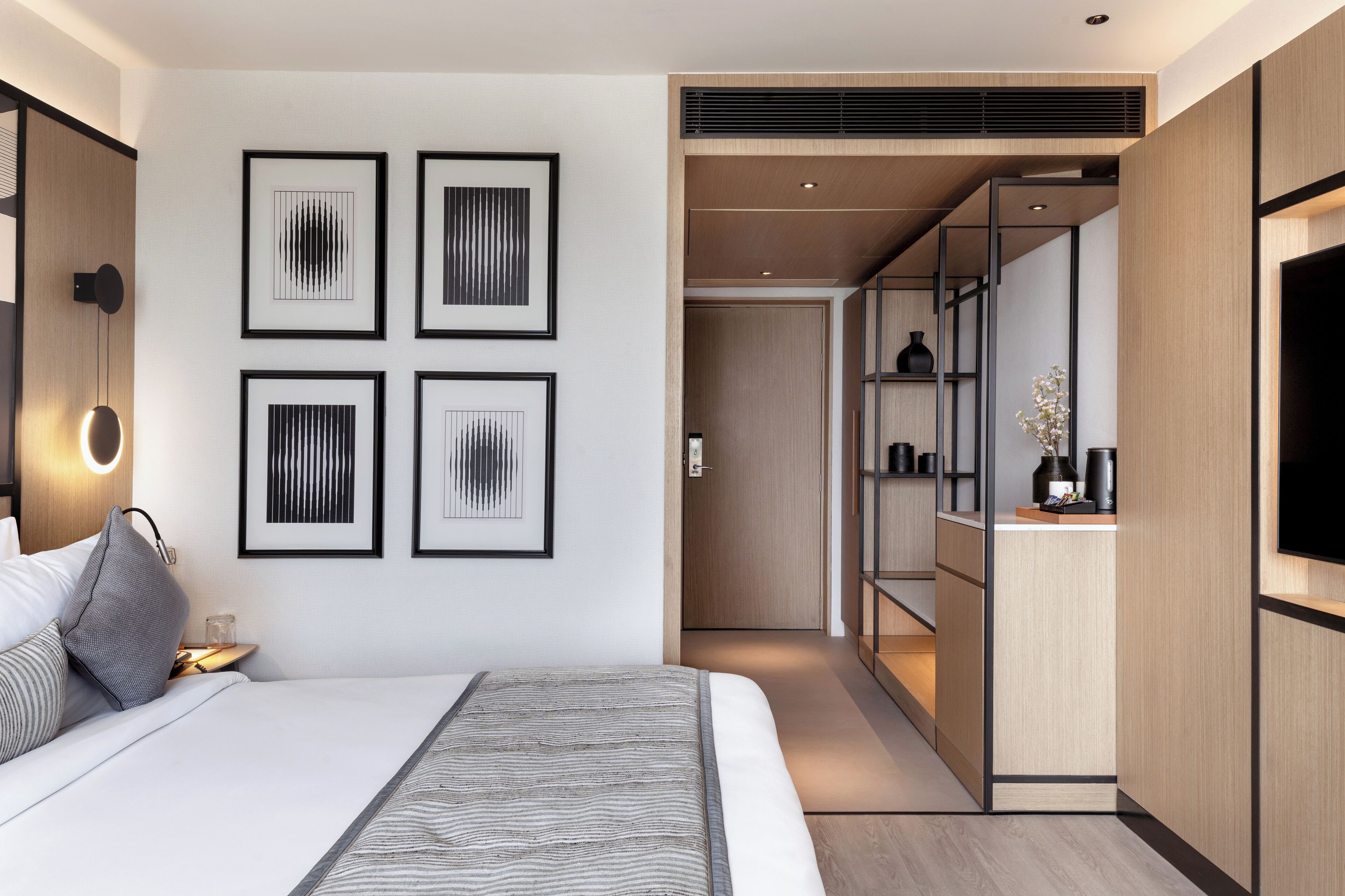 A modern hotel room with a large bed, a bedside table, a wall-mounted TV, and framed artwork.