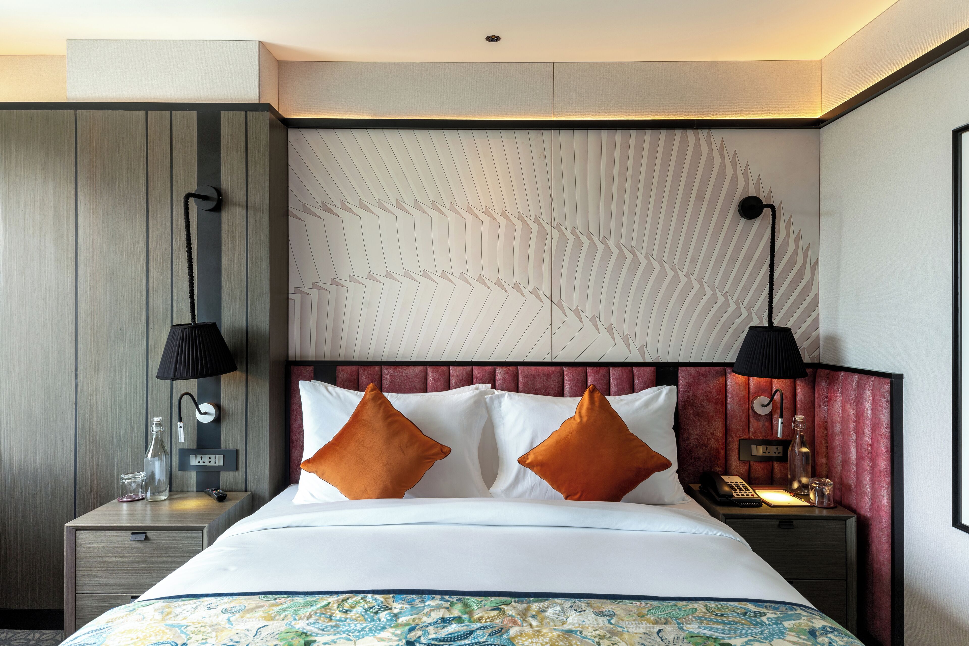 Une chambre d’hôtel avec un lit, deux tables de chevet, un panneau mural et un luminaire au plafond.