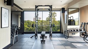 A modern gym with a squat rack, bench press, and kettlebells, large windows with a city view, and a mirror on the wall.