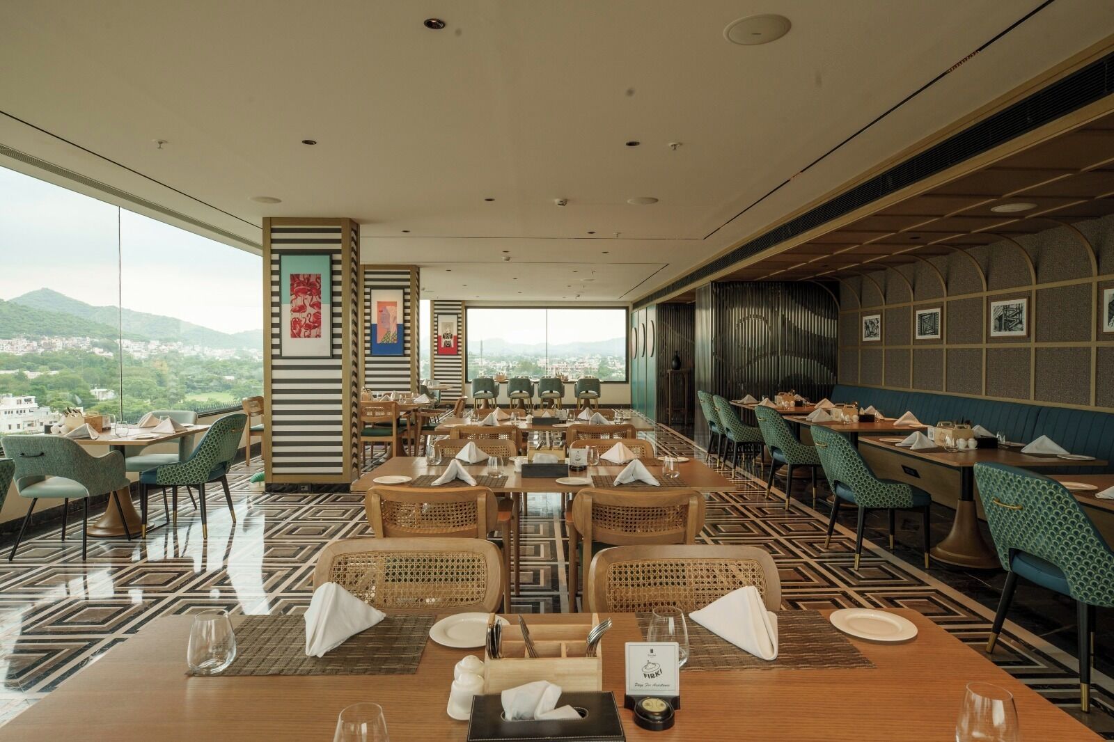 A restaurant with a panoramic city view, featuring a mix of wooden and rattan furniture, and a patterned floor.