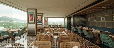 A restaurant with a panoramic city view, featuring a mix of wooden and rattan furniture, and a patterned floor.