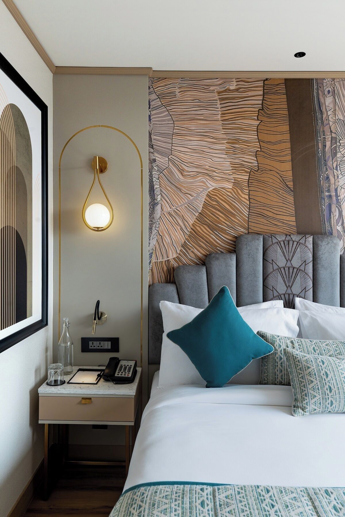 A modern hotel room with a large bed, a bedside table with a lamp, and a wall with a textured pattern.