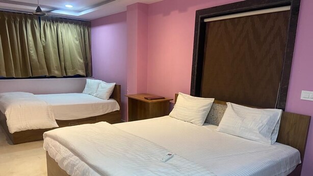 A hotel room with two beds, a wooden headboard, a nightstand, and a window with curtains. - Hotel Bablu Yadav (Maheshwaram)
