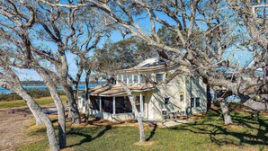 A two-story house with a porch, surrounded by trees and a body of water in the background. - Large WATERFRONT River House, Boater's Paradise! Brand New Dock, Walk to Beach, 1 mile to Boat Ramp (Saint Augustine)