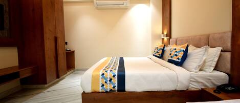 A hotel room with a wooden bed frame, a marble floor, a ceiling fan, an air conditioning unit, and a bedside table with a phone.