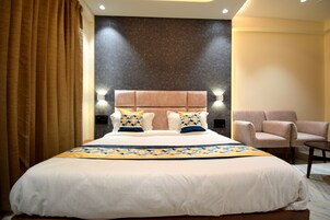 Habitación de hotel con una cama grande, dos lámparas de noche, un cabecero y una zona de estar con dos sillones.