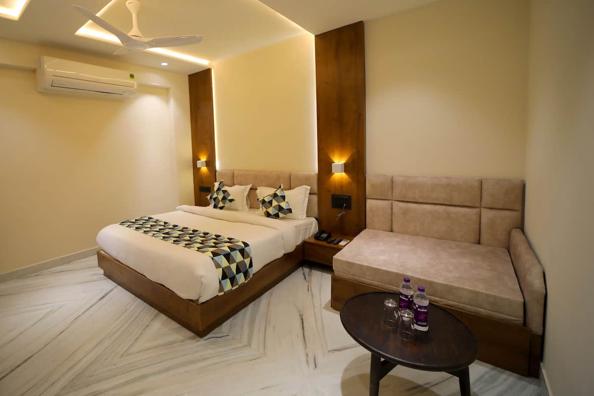 Une chambre d’hôtel avec un lit, un canapé, une petite table avec des bouteilles, un climatiseur et un ventilateur de plafond.