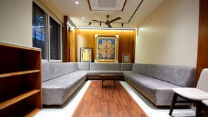 A modern living room with a sectional sofa, a wooden coffee table, and a bookshelf. - The Sky Imperial Hotel Sugam (Nathdwara)