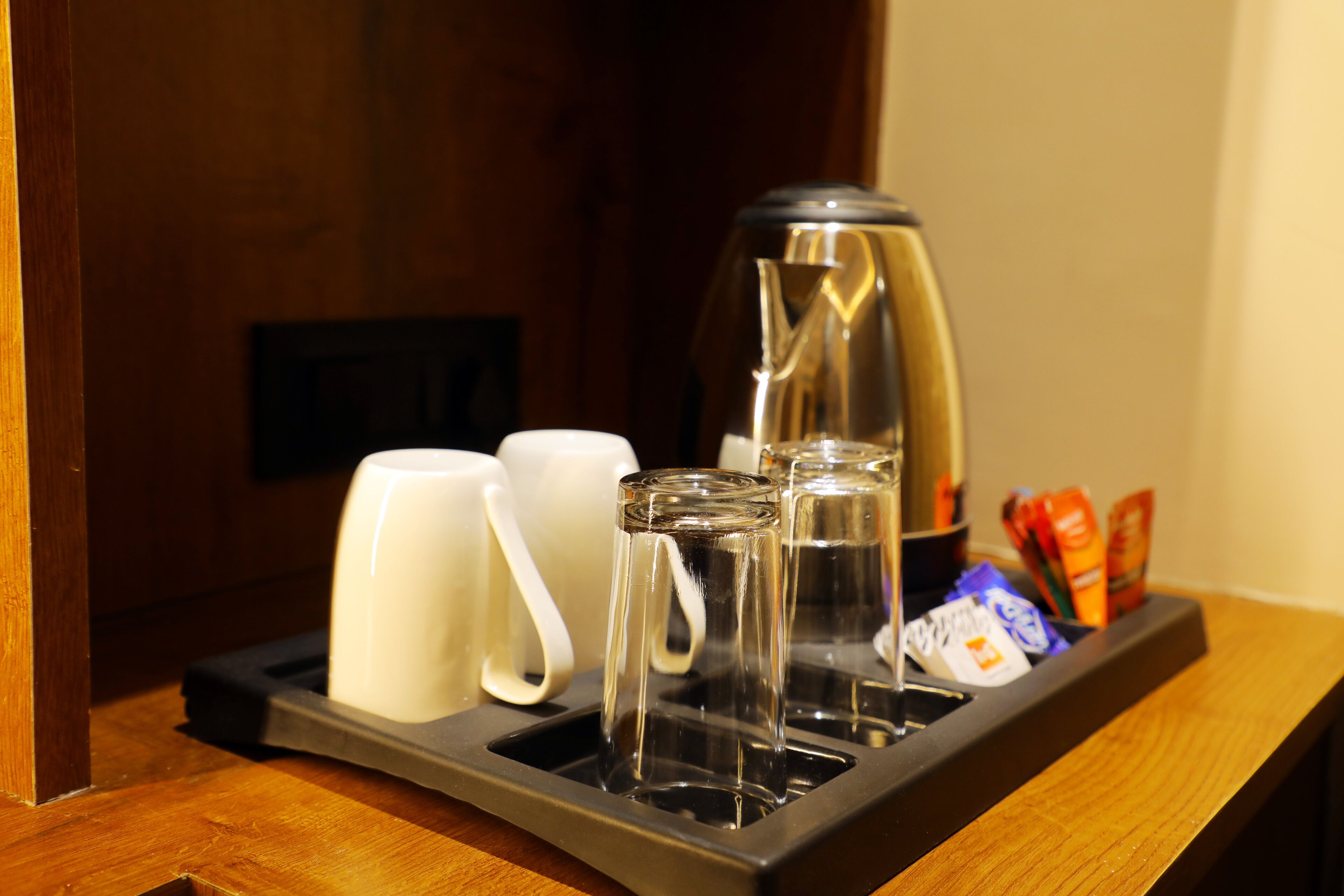 A tray with a coffee maker, two white mugs, a glass, and some snacks.