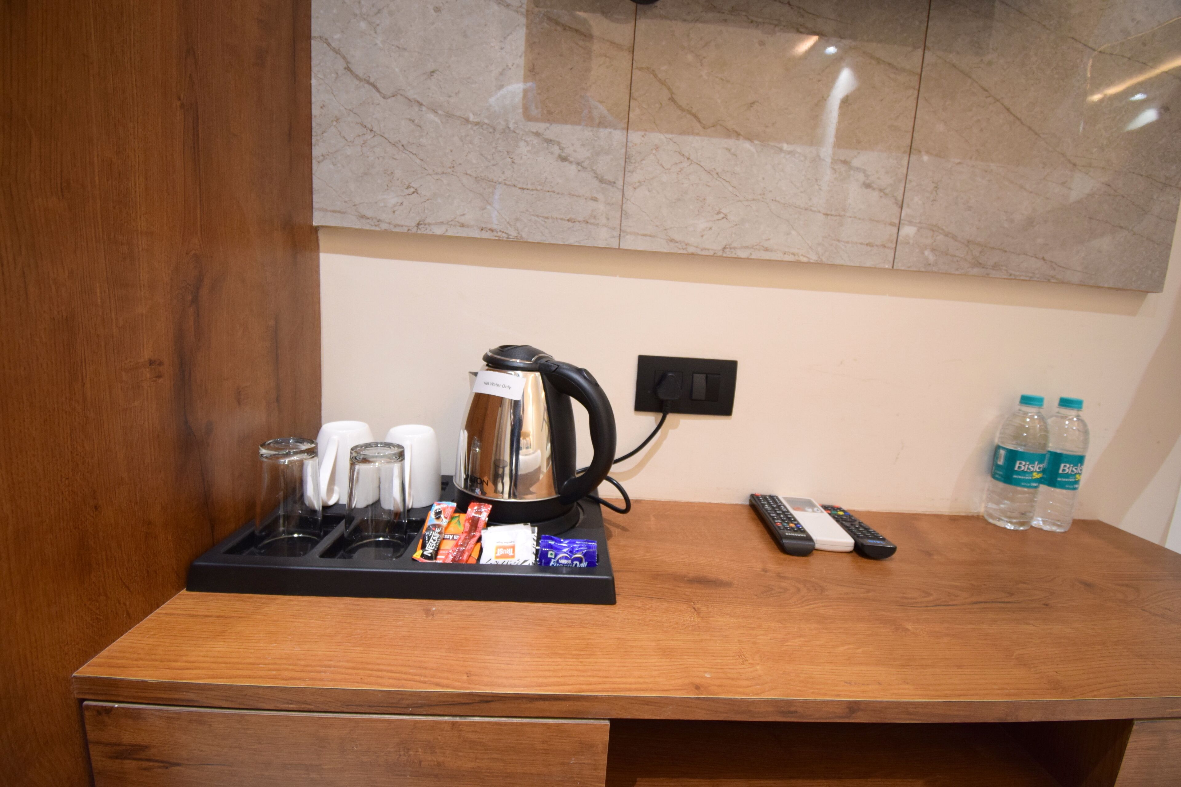 A wooden desk with a coffee maker, cups, snacks, and a remote control.