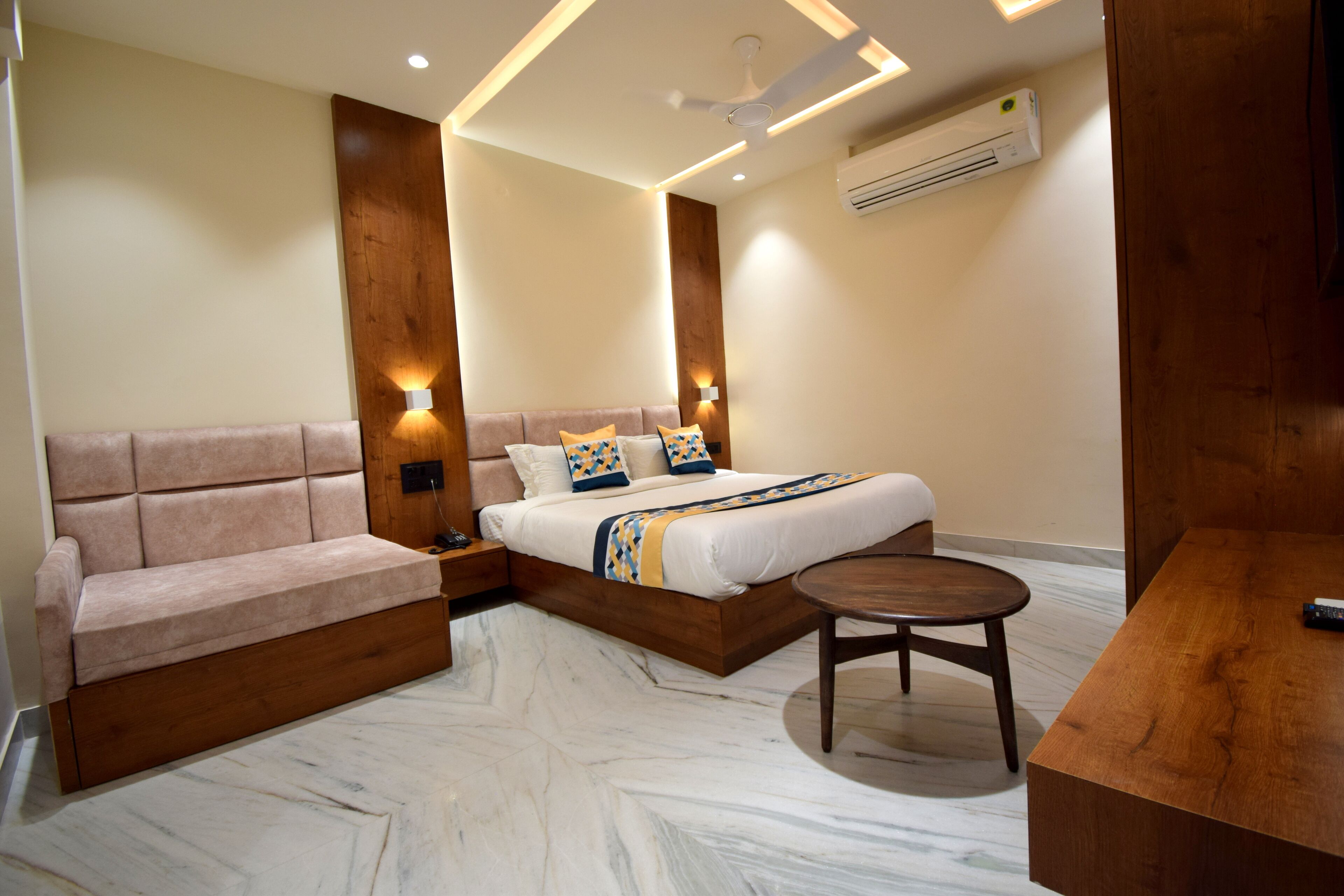A modern hotel room with a sofa, a bed, a round table, and a ceiling fan.