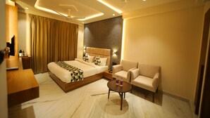 A modern hotel room with a large bed, a sofa, a coffee table, and a desk. - The Sky Imperial Hotel Sugam (Nathdwara)