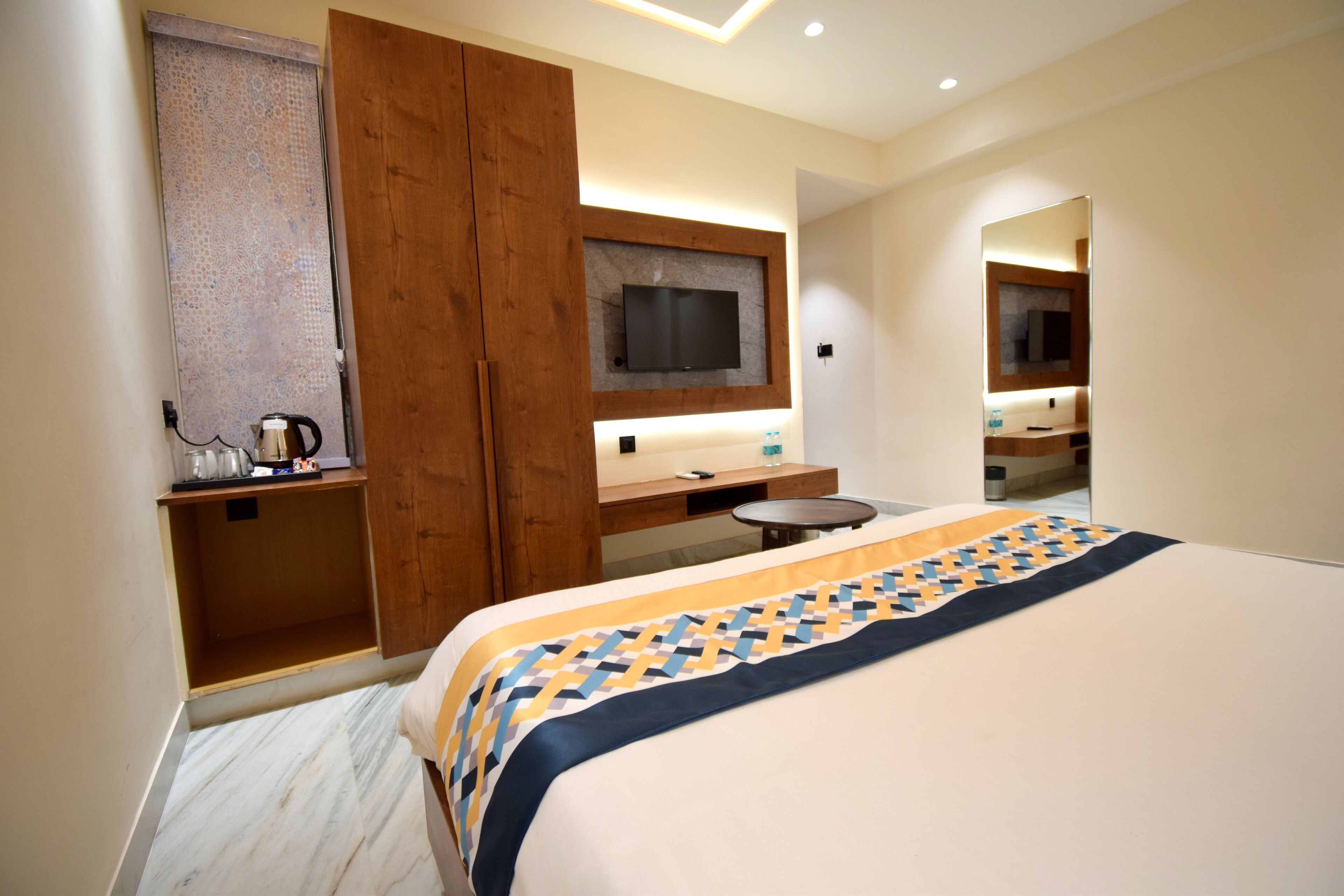 Ein Hotelzimmer mit Bett, Wandfernseher, Holzschrank, kleinem Tisch und Spiegel.