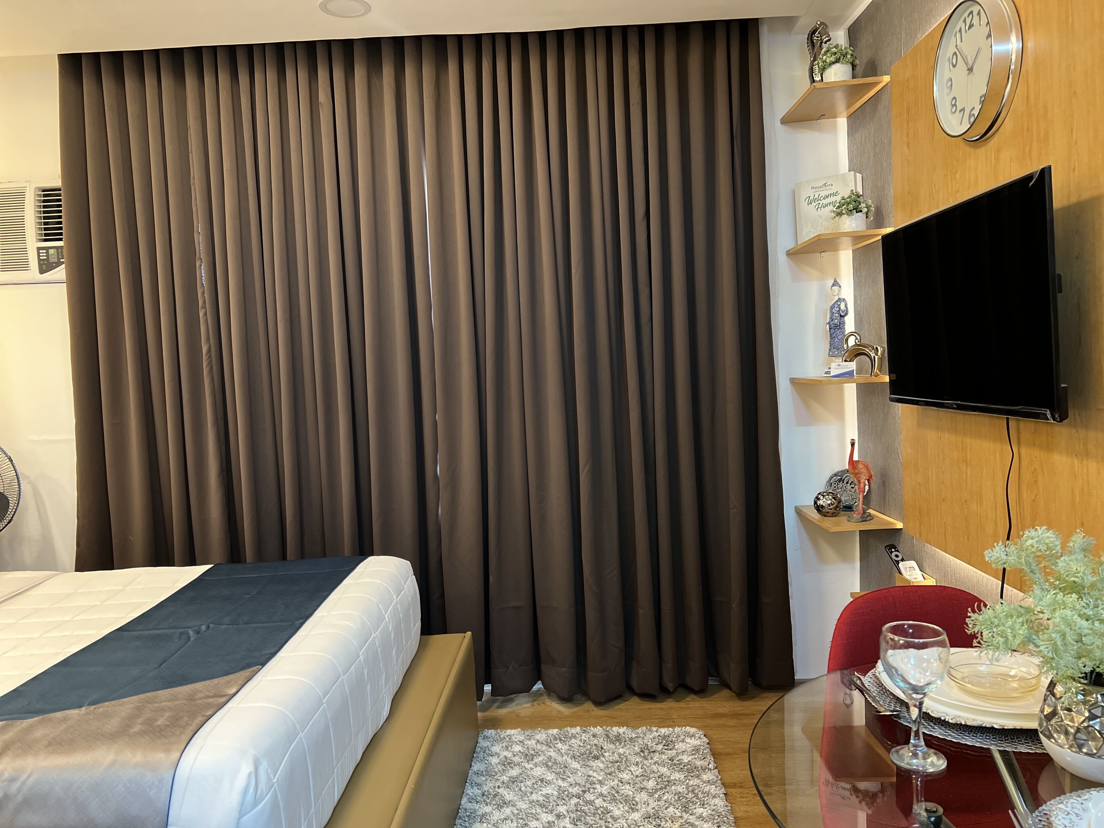 Ein modernes Hotelzimmer mit einem großen Bett, einem flachbildfernseher an der Wand, einem kleinen Tisch mit Glasplatte und einer Zierpflanze.