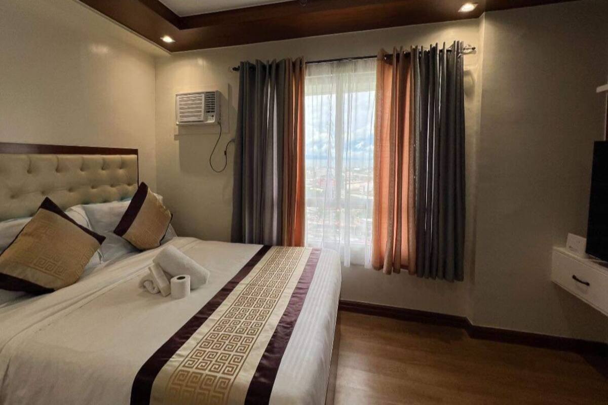 A hotel room with a large bed, a TV, and a window with curtains.