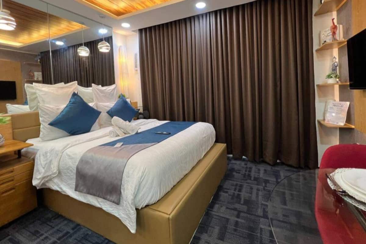 A modern hotel room with a large bed, a desk, a red chair, and a flat-screen TV.