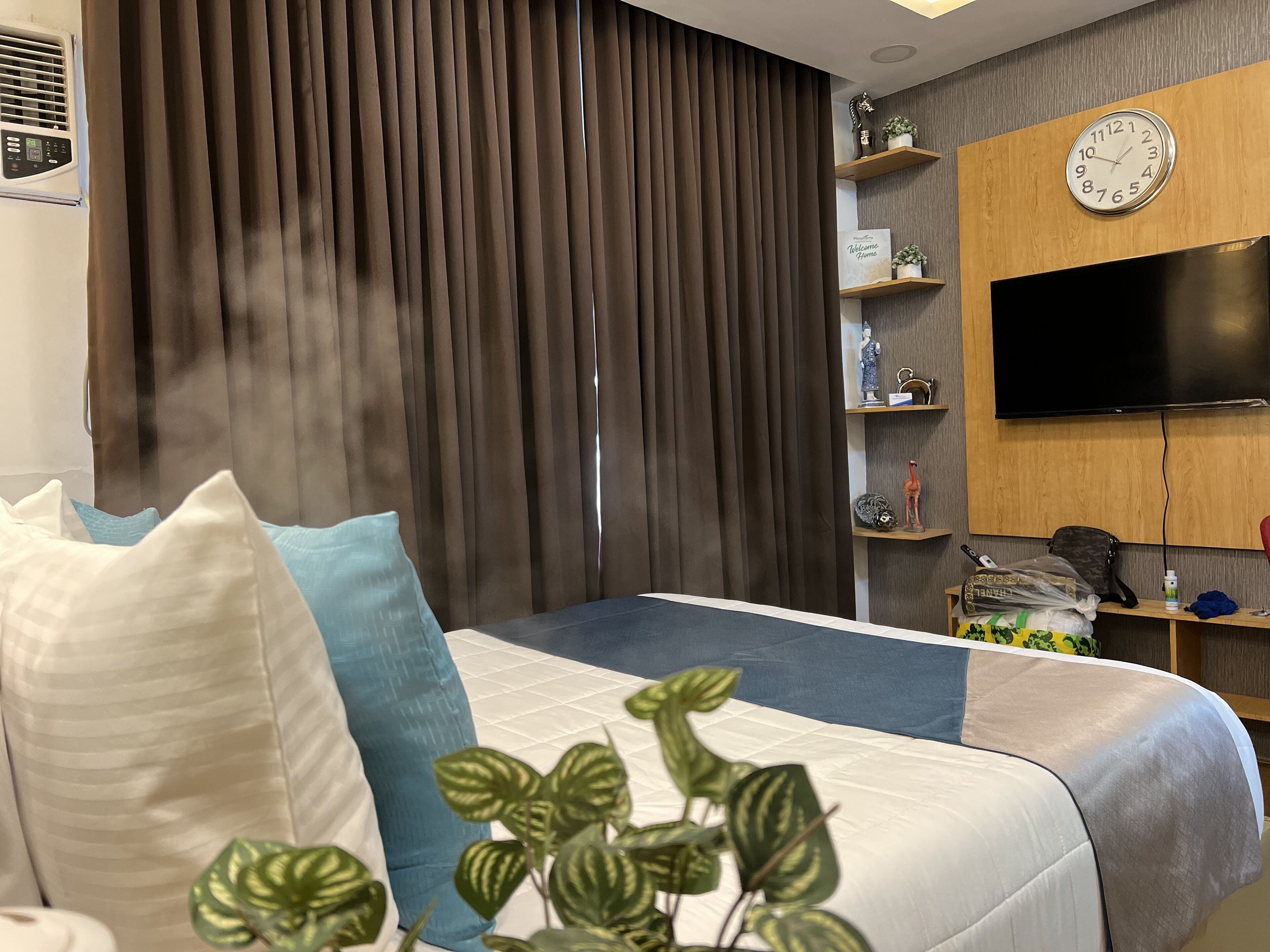 A modern hotel room with a large bed, a TV mounted on the wall, and a window with dark curtains.