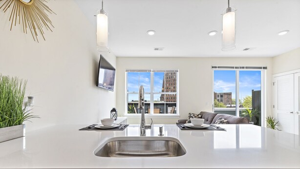 A modern kitchen with a central island, stainless steel sink, and a large window offering a view of buildings.