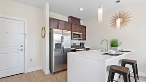 A modern kitchen with stainless steel appliances, a central island, bar stools, and a decorative sunburst light fixture.