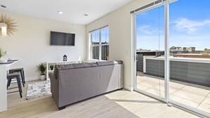 A modern living room with a grey sofa, a flat-screen TV, and a dining area with a table and chairs.