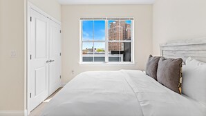 A bedroom with a large window, a bed with white bedding, and a wooden headboard.