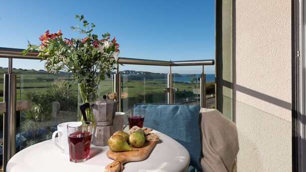 A balcony with a table set for a meal, a vase of flowers, and a view of a green landscape.