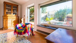 Una habitación con un ventanal grande, un aparador de madera y una manta colorida en una silla.