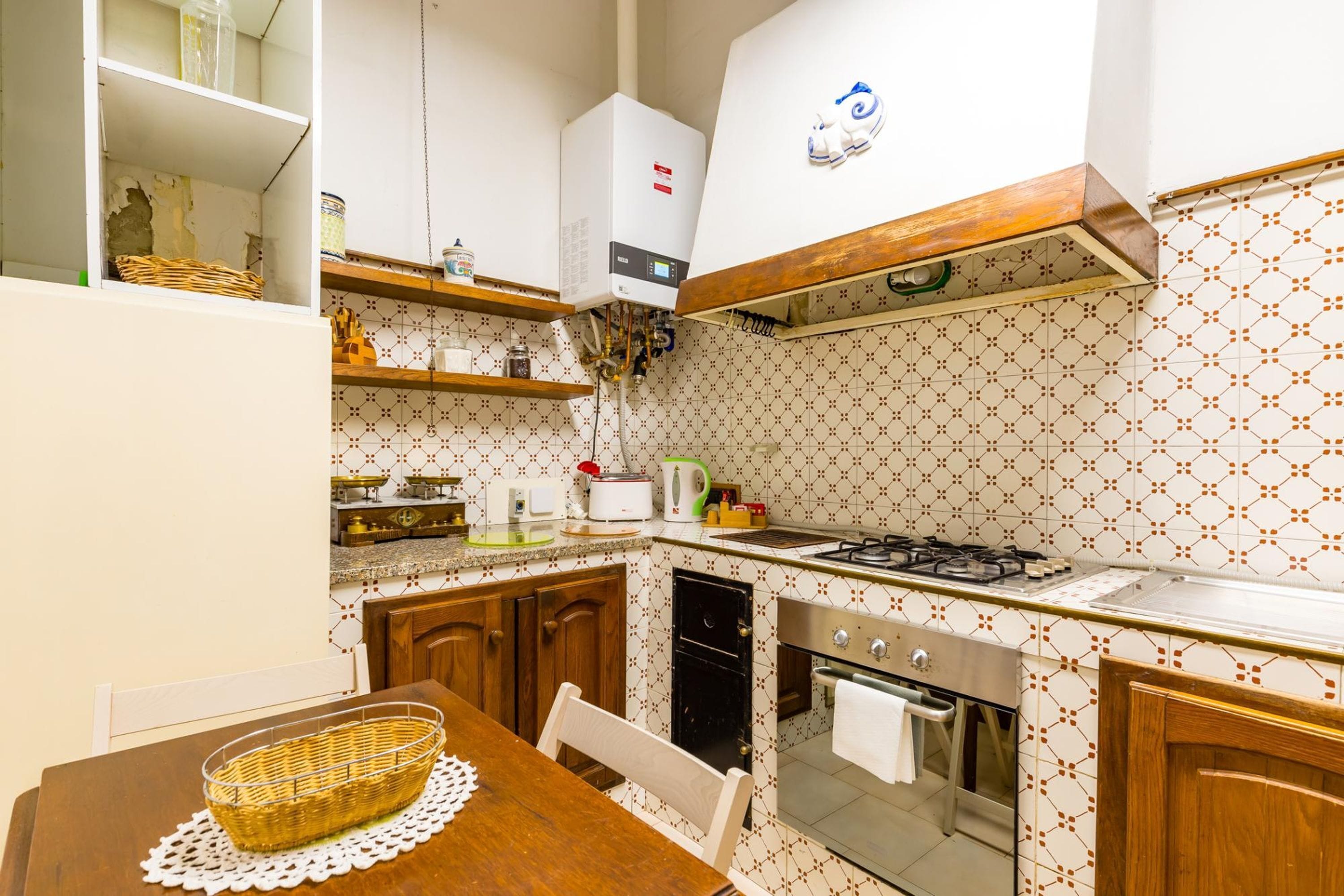 Une cuisine compacte équipée d’une cuisinière, d’un four et d’un chauffe-eau. On y trouve une table à manger avec un panier et une chaise.