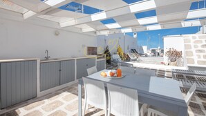 A covered outdoor area with a table set for dining, a kitchen area, and a stone wall. - TD Casa Altomare w Terrace Over Historic Center (Monopoli)