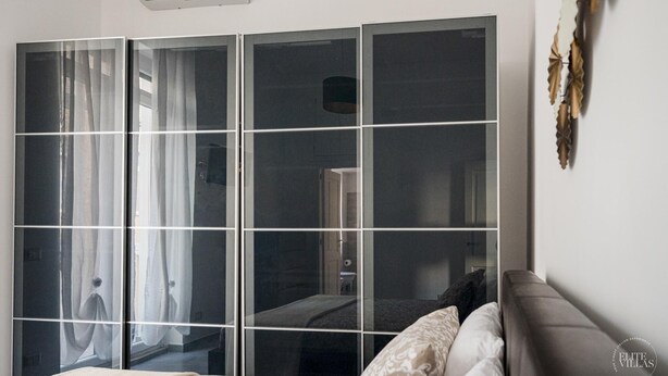A bedroom with a large sliding door closet, a bed with patterned bedding, and a wall-mounted air conditioner. - Poerio 98 Luxury Apartment (Naples)